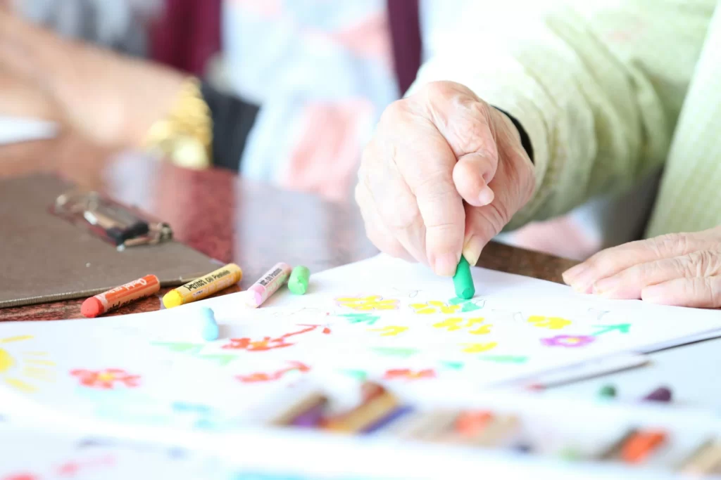 Person malt mit Wachsmalstiften während einer Kunsttherapiesityung